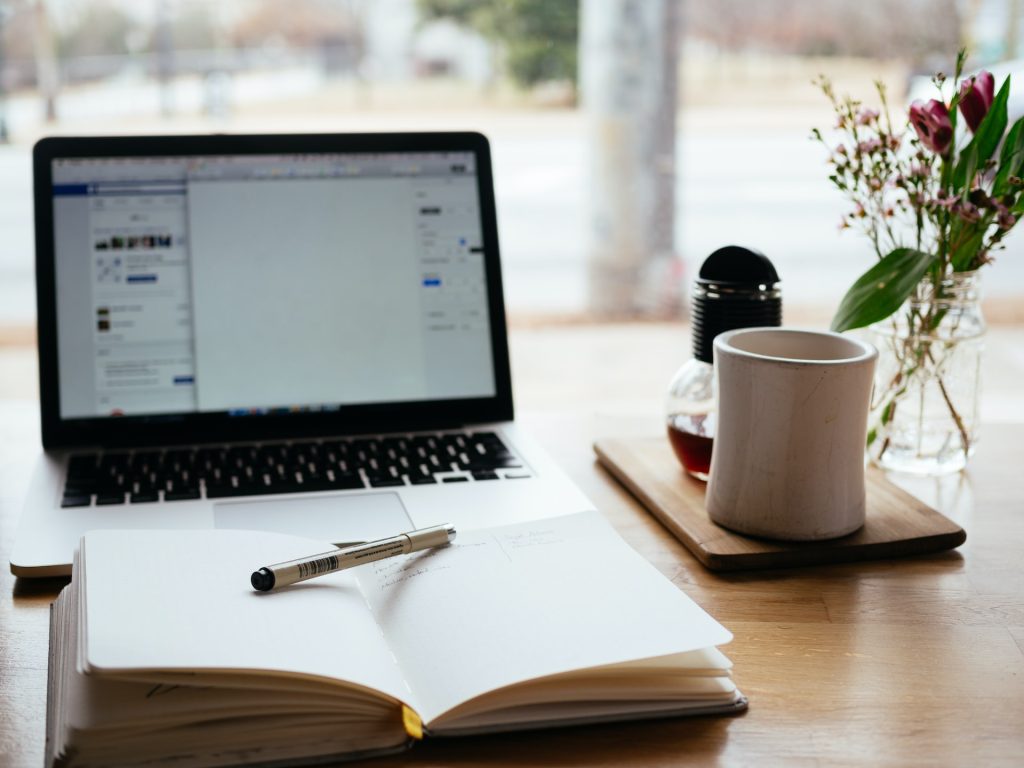 7 Practical Tips To Get New Clients For Your Aesthetics Business 2 An aesthetics practitioner’s desk with an open laptop, notebook, and pen, representing social media promotion and business planning.