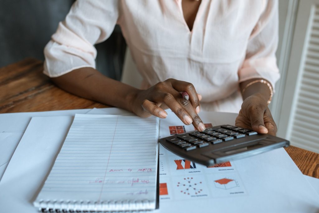 How To Offer Financing In Your Aesthetic Clinic 2 offer financing, black woman with a calculator with stacks of paper in a desk.