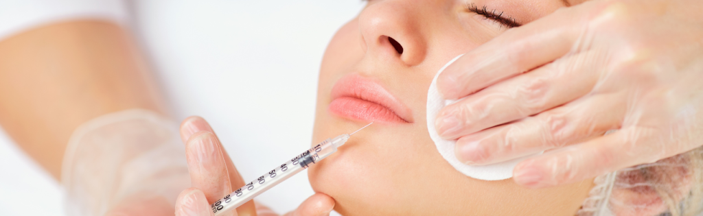 Dermal Fillers 101: What You Need to Know Before Your Appointment 1 dermal fillers being injected in the lips with the practitioner holding a piece of round cotton in the clients face.