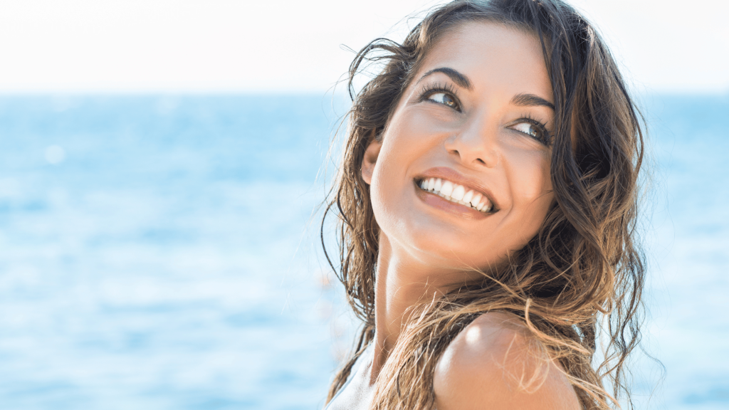 Botox vs. Fillers: The Perfect Summertime Treatment for Youthful Skin 1 a young woman smiling in front of the beach